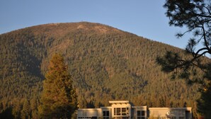 A modern building with a flat roof and large windows, surrounded by a well-maintained lawn and sand bunkers, with a forested hill in the background. - Your home away from home at Black Butte Ranch! (Sisters)