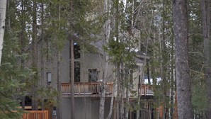A multi-story cabin surrounded by tall pine trees with a wooden deck and a small porch. - Your home away from home at Black Butte Ranch! (Sisters)