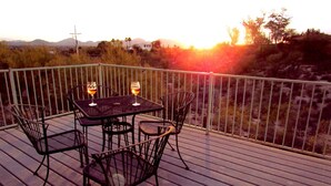 A deck with a table and chairs, overlooking a landscape with hills and a sunset. - Unique Retreat - Airstream in Central Location - Remote Feeling. (Tucson)