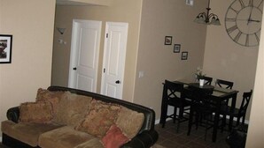 Ein Wohnzimmer mit einer Couch, einem Esstisch mit Stühlen, einer Wanduhr und zwei weißen Türen.