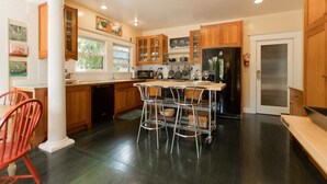 A kitchen with wooden cabinets, a black refrigerator, and a dining area with metal chairs. - The Napa Art House - w/fireplace & hot tub Near Downtown Napa (Napa)
