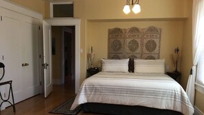 A bedroom with a large bed, a wooden floor, a decorative headboard, and a nightstand with a lamp. - The Napa Art House - w/fireplace & hot tub Near Downtown Napa (Napa)
