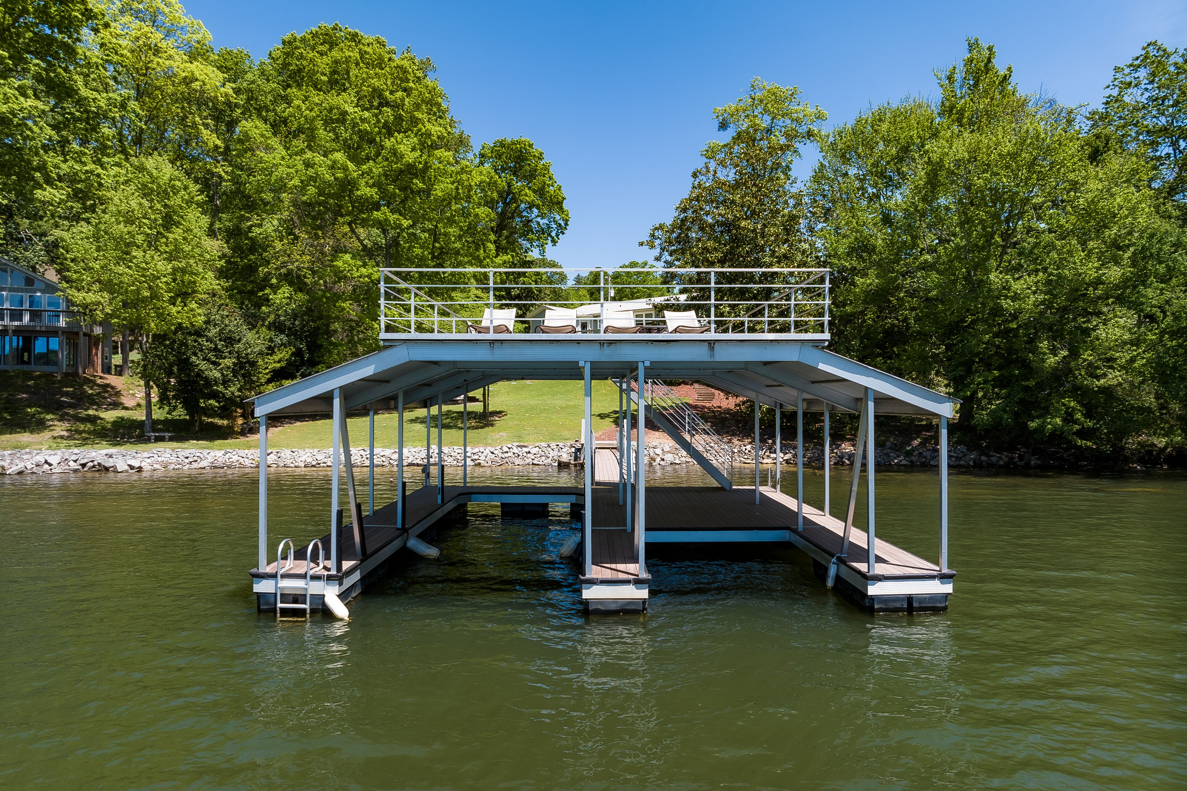 Ein überdachter Steg mit Liegestühlen und einer kleinen Brücke über dem Wasser, umgeben von Bäumen.