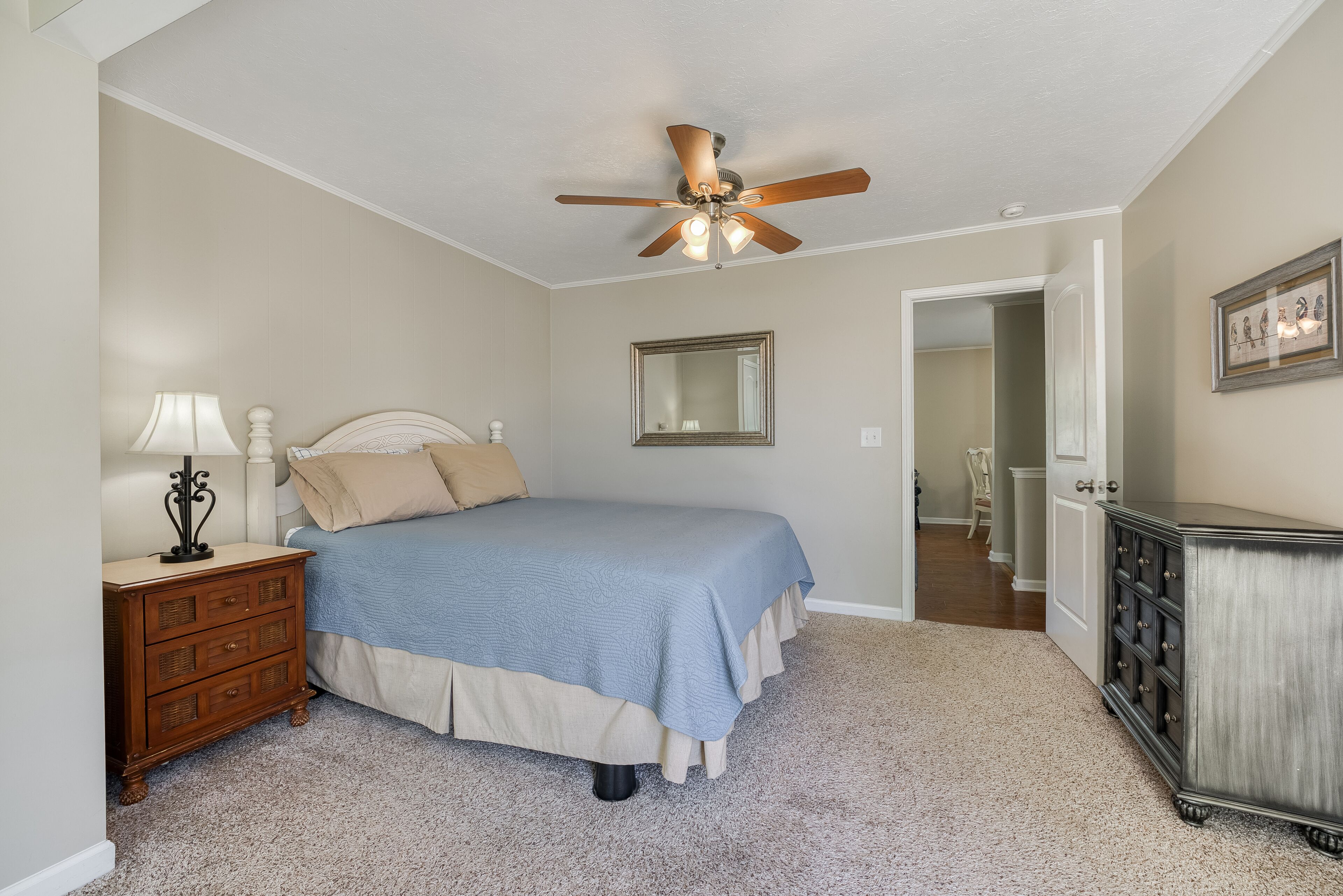 A bedroom with a bed, dresser, nightstand, ceiling fan, and a mirror on the wall.