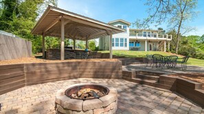 A covered patio area with a fire pit, outdoor seating, and a view of a two-story house. - Fabulous views on nice cove! Easy short walk to dock. Outdoor kitchen & fire pit (Gainesville)