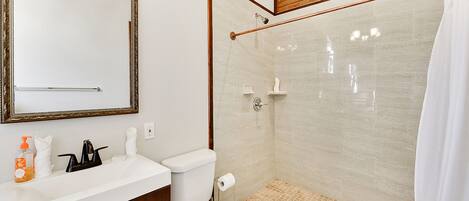 A bathroom with a white sink, a mirror, a toilet, and a shower area.