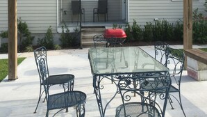 A covered patio with a glass table and metal chairs, a red grill, and a house in the background. - 4 bedroom with Swimming Pool,  NEAR FRENCH QUARTER- (Arabi)