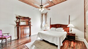 A bedroom with a wooden ceiling, a bed with white linens, a wooden nightstand with a lamp, a wooden chair, and a wooden cabinet with a mirror. - 4 bedroom with Swimming Pool,  NEAR FRENCH QUARTER- (Arabi)