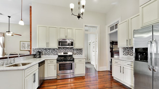 A modern kitchen with white cabinets, stainless steel appliances, a wooden floor, and a chandelier. - 4 bedroom with Swimming Pool,  NEAR FRENCH QUARTER- (Arabi)