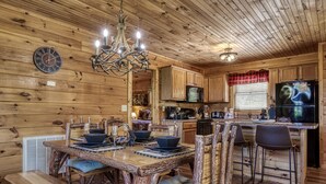 A rustic wooden interior with a dining table set for four, a bar area, and a kitchen with wooden cabinets and a large TV. - Mountain and Ferris Wheel View,wifi and Close to Pigeon Forge (SEVIERVILLE)