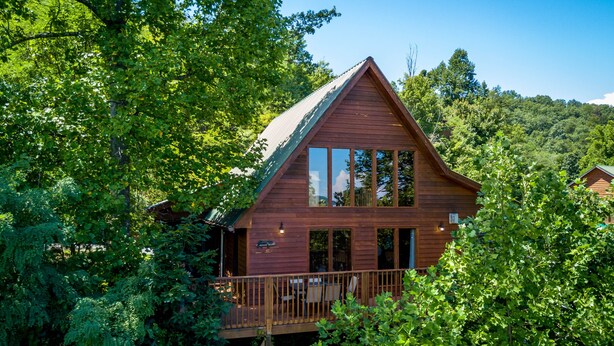 A wooden cabin with a balcony, surrounded by dense greenery. - Mountain and Ferris Wheel View,wifi and Close to Pigeon Forge (SEVIERVILLE)