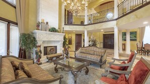 Amplia sala de estar con un imponente candelabro, una chimenea y varios conjuntos de asientos, incluyendo sofás y sillones.