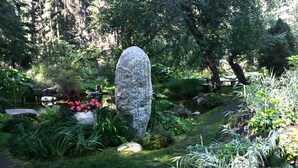 A garden with a large stone structure, lush greenery, and a small pond. - Huckleberry Hideaway: Authentic Cabin Adventure, steps away from Payette Lake (McCall)
