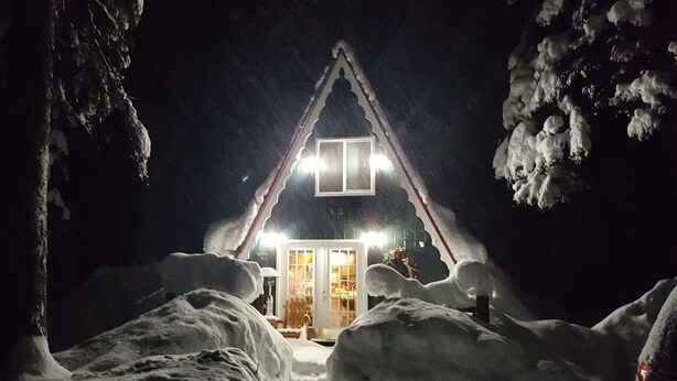 A snow-covered landscape with a triangular structure featuring a lit entrance and a window. - Huckleberry Hideaway: Authentic Cabin Adventure, steps away from Payette Lake (McCall)