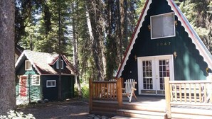 A cabin with a wooden porch and a door, surrounded by trees. - Huckleberry Hideaway: Authentic Cabin Adventure, steps away from Payette Lake (McCall)