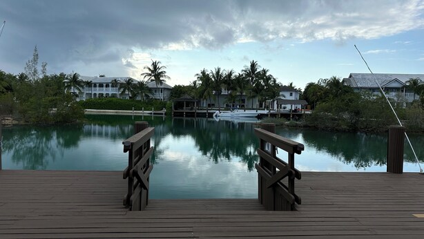 A wooden dock with a view of a calm water body, a boat docked, and a row of houses in the background. - Luxurious 'Old Fort Bay' Large SINGLE LEVEL with 4 bedrooms each with an ensuite (Old Fort Bay)