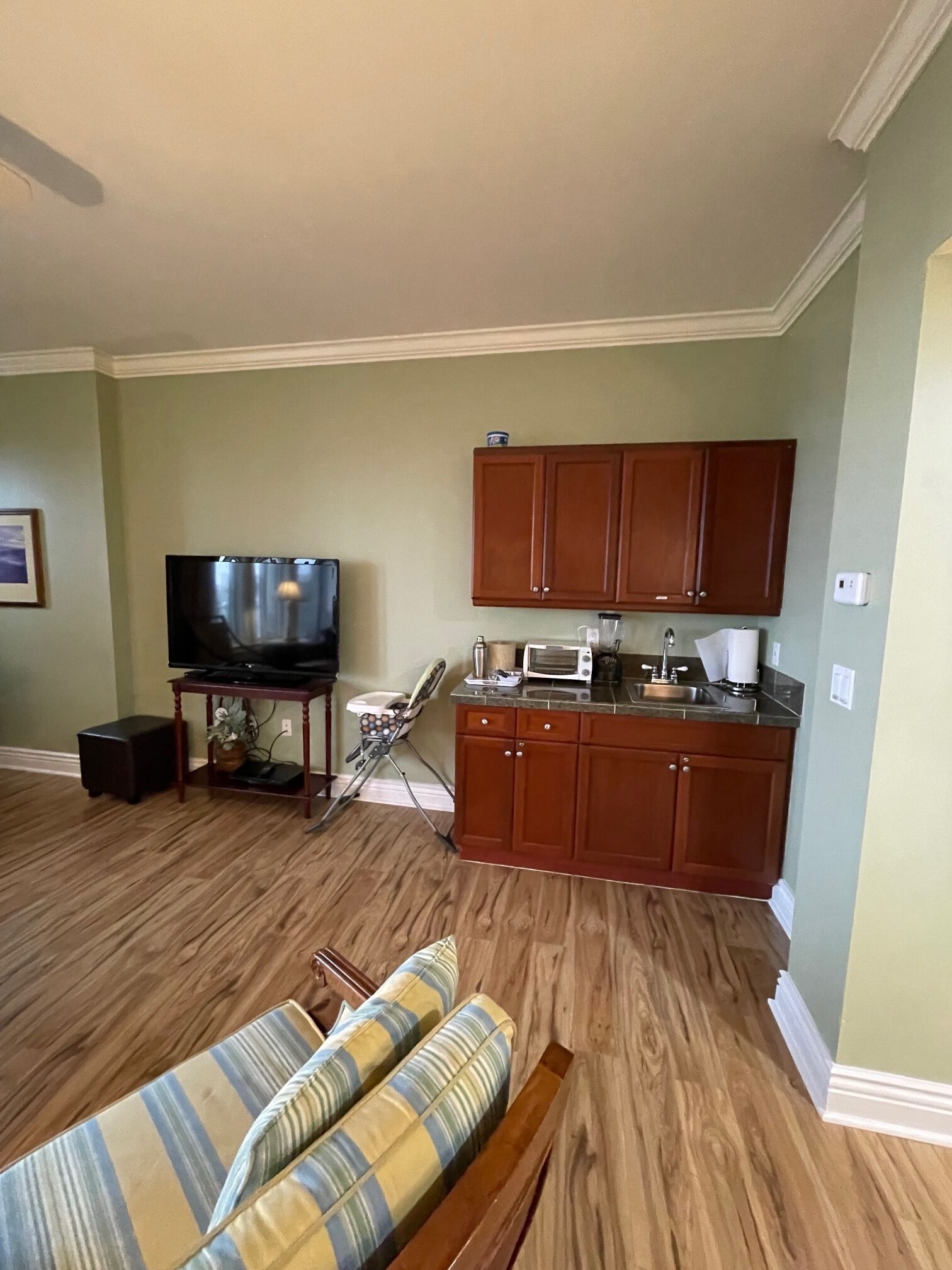 A living room with a television, a sofa, and a kitchen area with wooden cabinets and a microwave.
