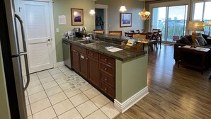 A spacious kitchen with a large island, wooden flooring, and a dining area with a view. - Bay views & sunsets in the Grand Sandestin! Baytowne Wharf Village (Destin)