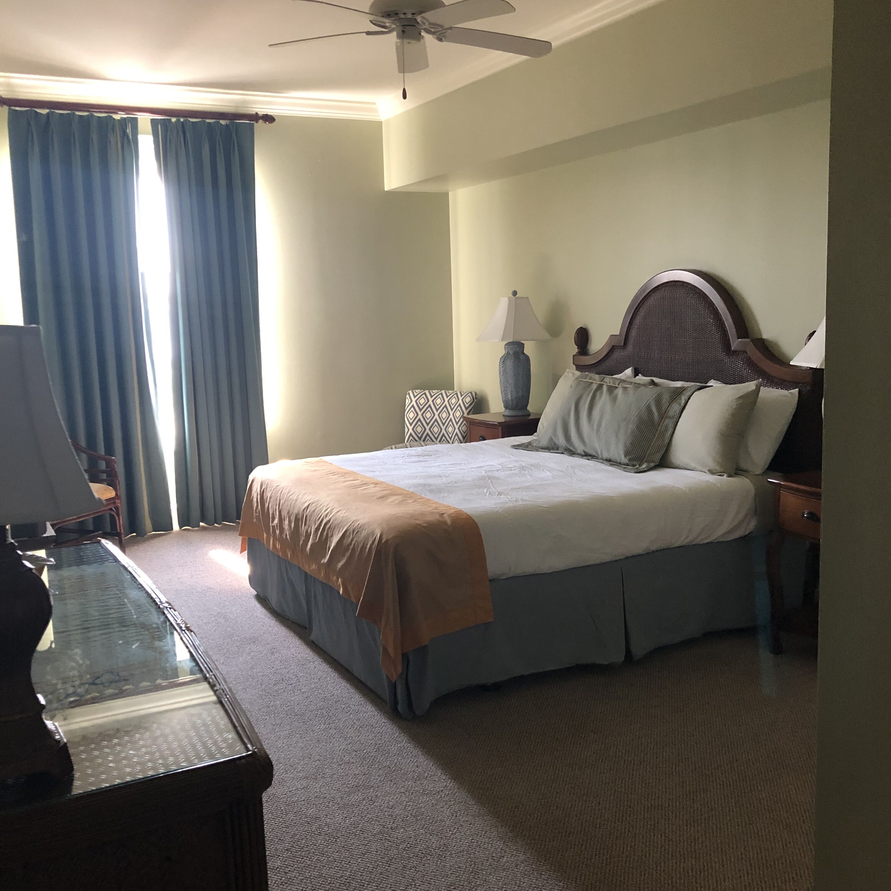 A hotel room with a bed, a desk, a chair, a lamp, and a ceiling fan.