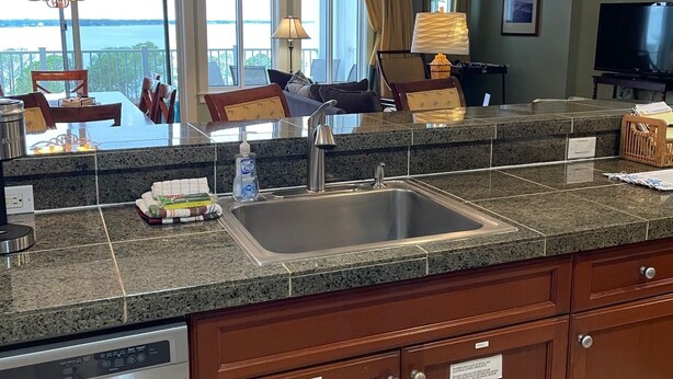 A modern kitchen with granite countertops, stainless steel appliances, and wooden cabinets. There is a large window offering a view of the outdoors. - Bay views & sunsets in the Grand Sandestin! Baytowne Wharf Village (Destin)