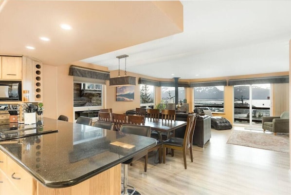 Una cocina moderna con una isla central, zona de comedor con sillas y un gran ventanal con vistas.