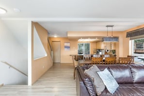 Una sala moderna con un sofá de cuero marrón, una mesa de comedor de madera y una cocina al fondo.