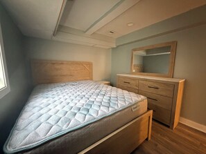 Quarto com cama, cômoda, espelho e janela.