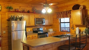 A wooden cabin kitchen with a refrigerator, microwave, stove, and a ceiling fan.