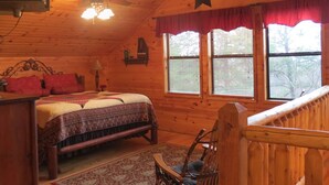 A cozy log cabin bedroom with a bed, a chair, a desk, and a window with blinds.