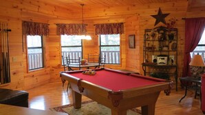 A wooden cabin interior with a pool table, a dining table, and a star decoration on the wall.