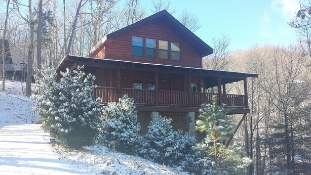 A wooden cabin with a balcony, surrounded by snow-covered trees and a clear sky.