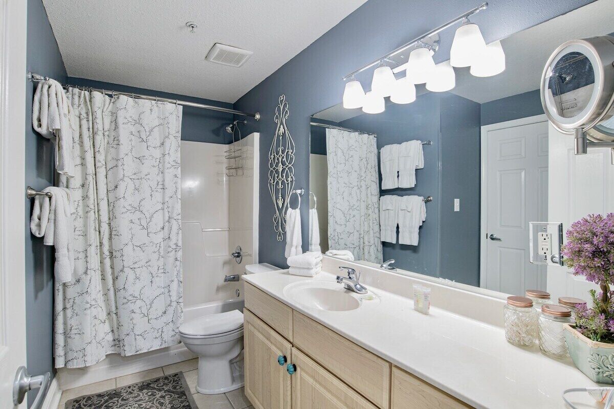 A modern bathroom with a shower, toilet, vanity, and a large mirror.