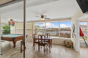 A sunroom with a pool table, chairs, a ceiling fan, and large windows offering a view of the outdoors.