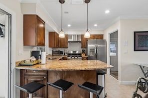 A kitchen with granite countertops, wooden cabinets, stainless steel appliances, pendant lighting, and a bar stool seating area.