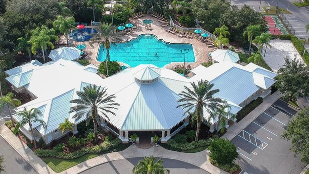 Une grande piscine entourée de chaises longues et de parasols, avec un bâtiment dont l’architecture distinctive, notamment la forme du toit, se détache au premier plan.