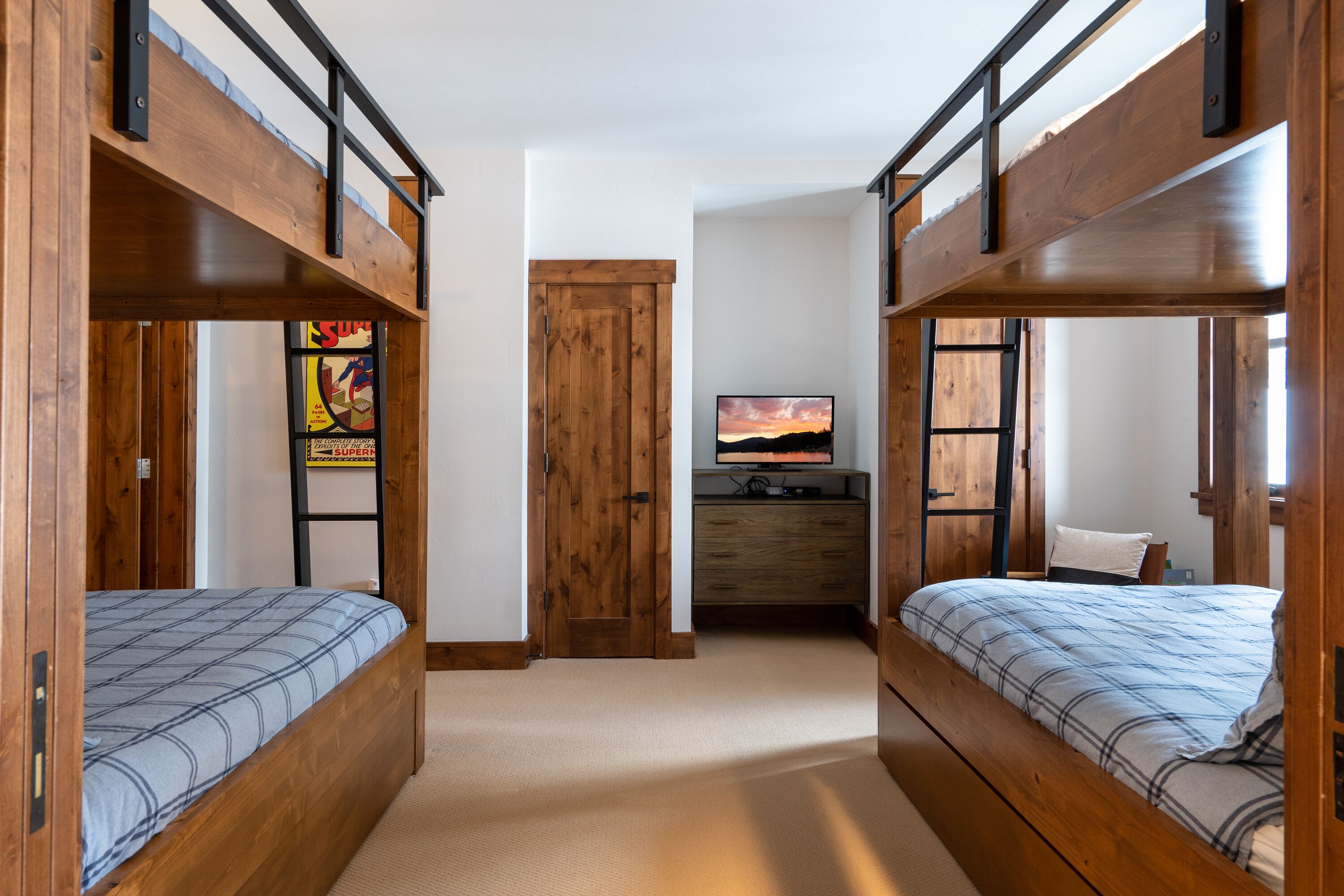 A room with two bunk beds, a wooden door, a television, and a small desk.