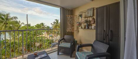 A balcony with wicker furniture, a small table with a decorative item, and a shelf with plants and decorative items.
