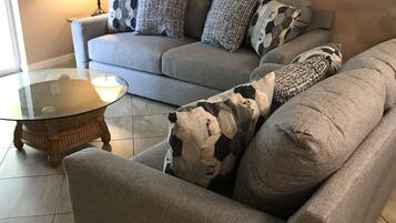 Un salon avec un canapé gris, une table basse en verre et des coussins à motifs.
