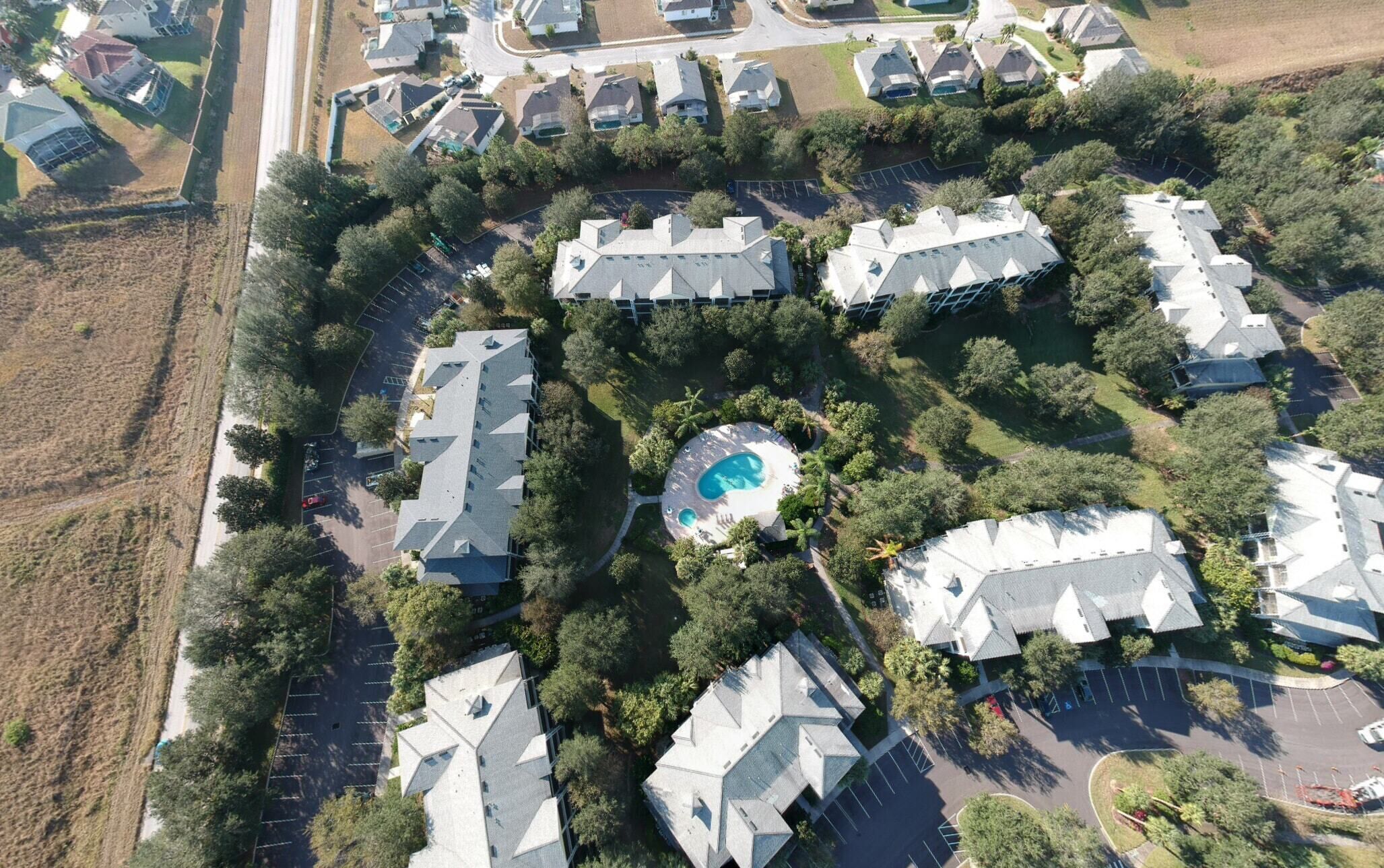 An aerial view of a residential area with multiple houses, a central swimming pool, and surrounding greenery.