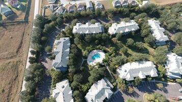 An aerial view of a residential area with multiple houses, a central swimming pool, and surrounding greenery.
