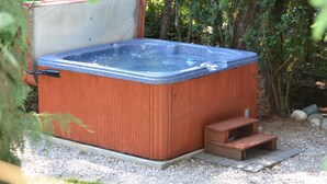 Un jacuzzi con revestimiento de madera y parte interior azul, rodeado de grava y follaje.