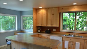 Una cocina con armarios de madera, una isla grande con taburetes de bar, lavavajillas integrado y ventana con vista a árboles.