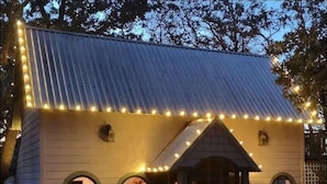 Une maison avec un toit en métal, une véranda dotée d’une balustrade et des guirlandes lumineuses disposées autour du toit.