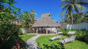 A thatched-roof hut with a garden path leading to a seating area with lounge chairs. - Casa Colibri - Los Delfines (Sayulita)