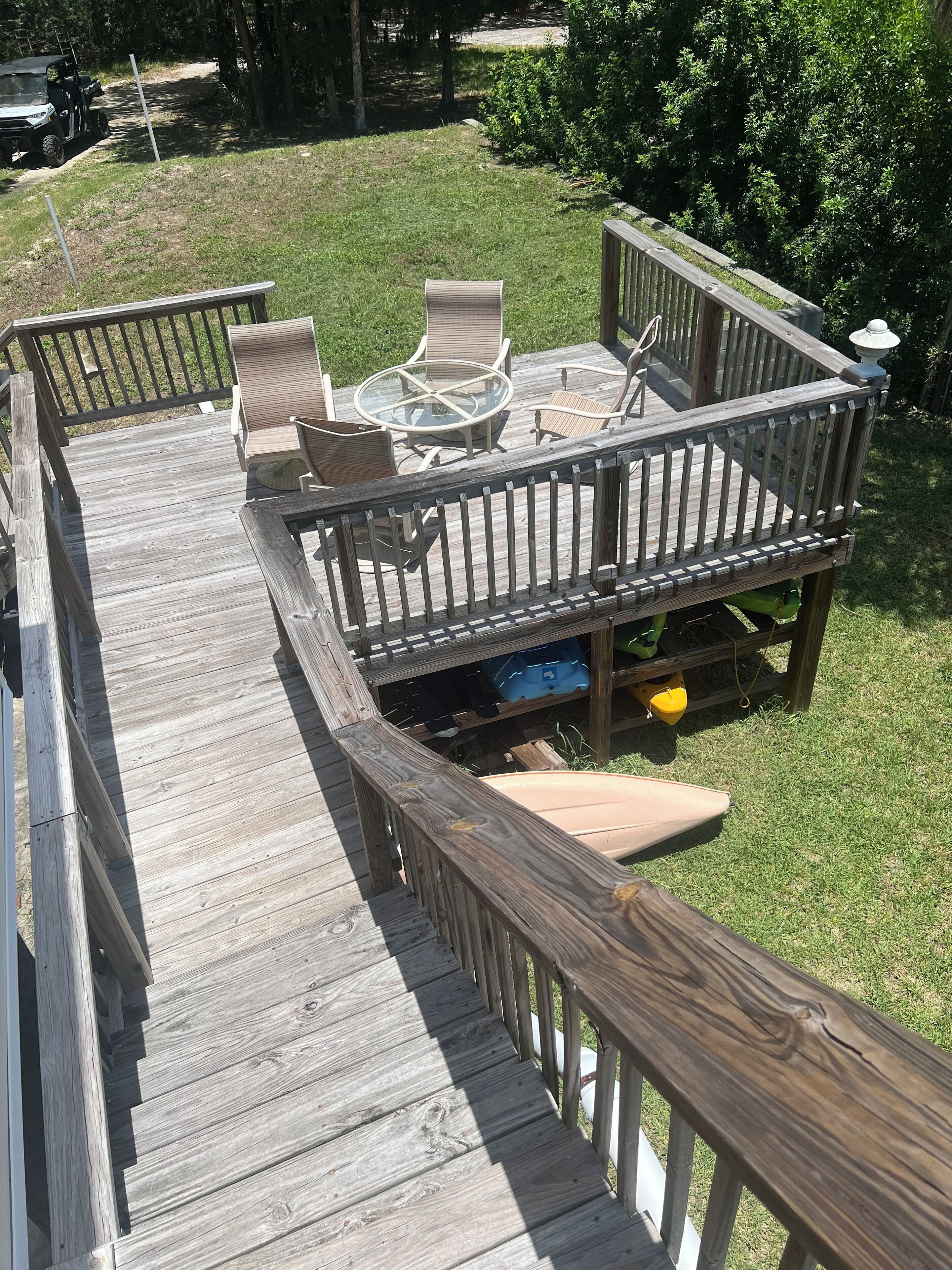 A wooden deck with a glass-top table and chairs, surrounded by a railing.