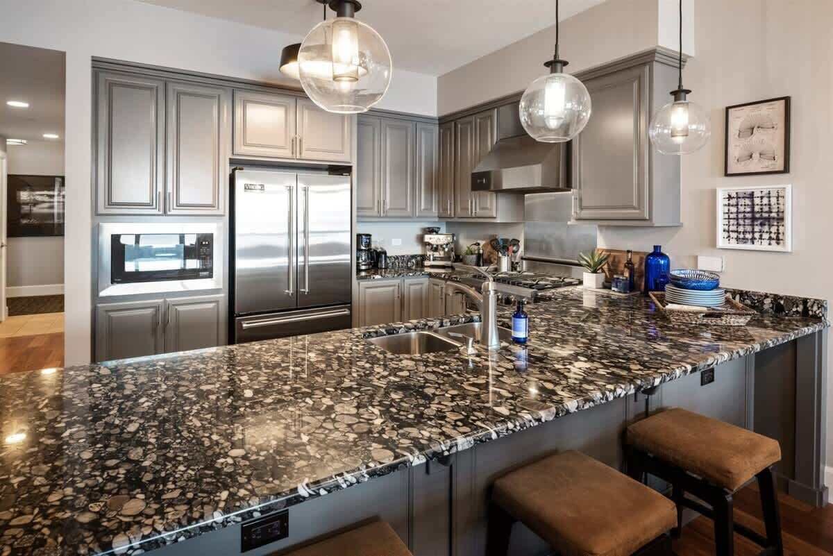 A modern kitchen with granite countertops, stainless steel appliances, and pendant lighting.