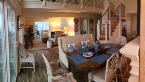 A spacious living room with a high ceiling, a dining area with a wooden table and chairs, and a staircase leading to an upper level. - Beach is 50 steps away and you have PRIVATE beach access and wonderful views (Folly Beach)