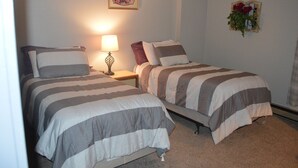 Een kamer met twee bedden, een nachtkastje met een lamp en een bloemstuk aan de muur.