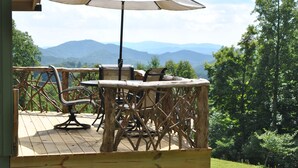 A wooden deck with outdoor furniture, including a table and chairs, overlooking a mountainous landscape.
