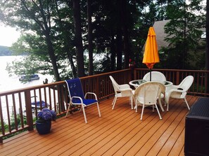Une terrasse en bois avec des chaises en osier blanc et une chaise bleue, une plante en pot et un parasol orange.